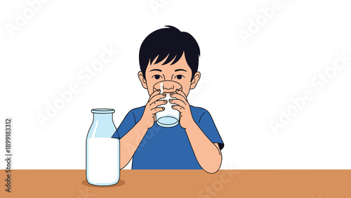 Young boy happily drinking a glass of fresh white milk while sitting at a wooden table with a full milk bottle.