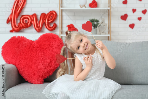 Cute little girl with paper hearts sitting in room decorated for Valentines Day