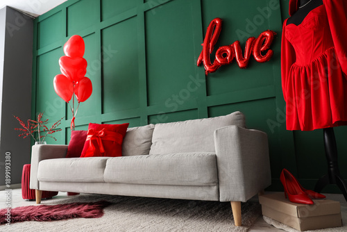Interior of festive living room with grey sofa, red dress on mannequin and decor for Valentine's Day celebration