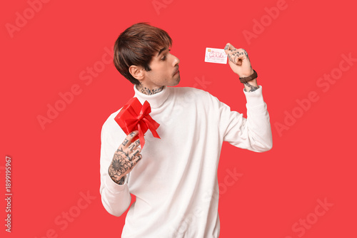 Handsome young man with gift box and credit card on red background. Valentine...