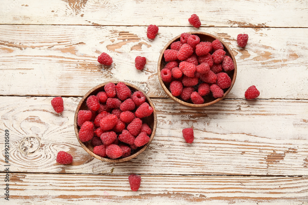 Naklejka premium Bowls with fresh raspberry on light wooden background