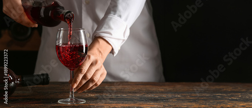 Foto Female bartender pouring red wine from bottle into glass, closeup