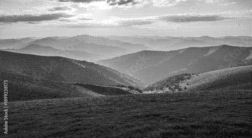 A serene black and white landscape photograph of rolling hills and mountains viewed from a high vantage point on a cloudy day