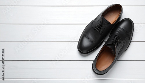 Pair of black leather shoes on white wooden floorboards viewed from above