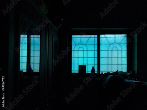 Bild auf Leinwand A darkened room with a mirror reflecting a clear view of a window covered in vibrant blue, translucent material, creating a moody, atmospheric scene used to evoke a sense of mystery or fear