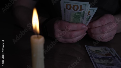 Under the soft, dancing light of a solitary candle, hands meticulously sort and stack crisp United States 100 dollar notes.