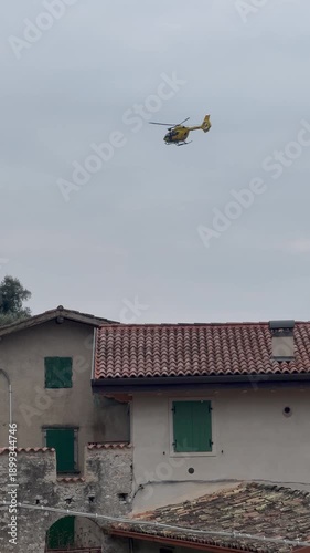 Rescue helicopter with medical team operating in the mountains near Lake Garda, Italy, performing emergency air rescue in a rugged alpine landscape.