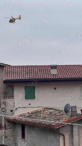 Rescue helicopter with medical team operating in the mountains near Lake Garda, Italy, performing emergency air rescue in a rugged alpine landscape.