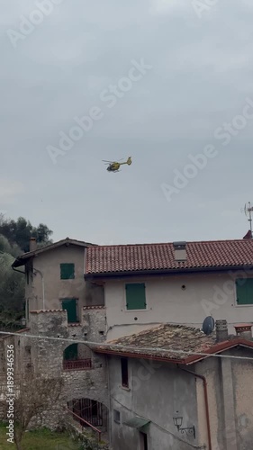 Rescue helicopter with medical team operating in the mountains near Lake Garda, Italy, performing emergency air rescue in a rugged alpine landscape.