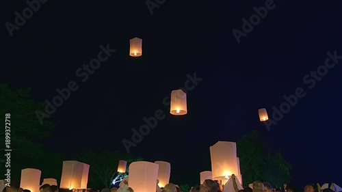 Beautiful floating lanterns rising into the dark night sky during Yee Peng Festival in Thailand. People releasing traditional paper lamps for luck and celebration.