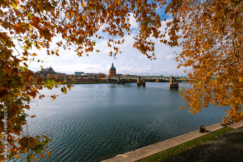 Autumn-colored trees frame the view of the Garonne River and the chapel of Saint Joseph de la Grave in the city of Toulouse, France.