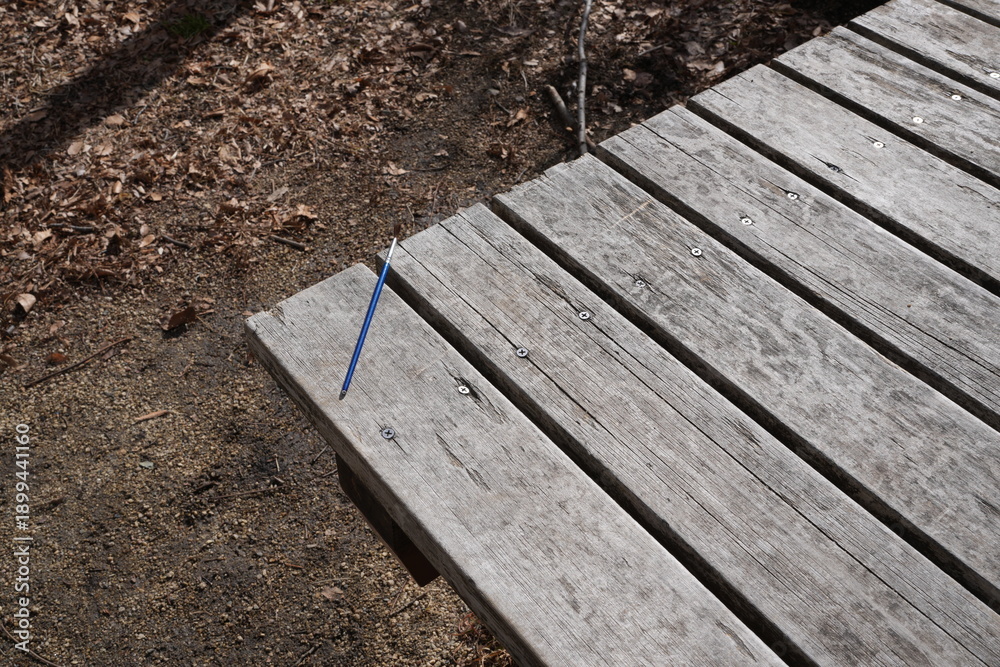 Fototapeta premium A wooden bench with a blue pencil on it. The bench is in a wooded area