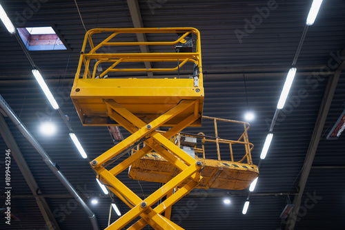 Foto Yellow aerial work platform scissor lift extended high indoors, low angle shot w