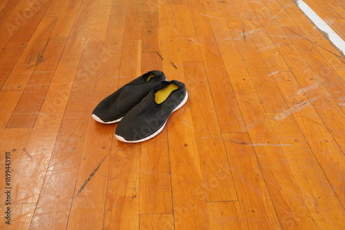 A pair of black shoes are laying on a wooden floor. The shoes are placed in a way that they are facing the camera. The image has a simple and minimalistic feel to it, with the focus being on the shoes