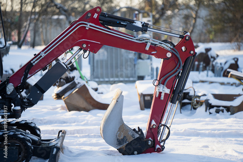 Foto Side view of compact excavator arm with red boom, hoses and bucket on snowy grou
