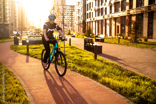 Billede på lærred Woman cyclist riding on red bike lane in modern city district during sunset