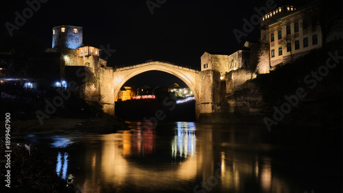 Low-angle view of historic stone bridge illuminated at night, reflected in calm river water. Old bridge in Mostar, Bosnia and Herzegovina