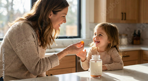 A happy mother and daughter share a healthy moment, feeding each other supplements at their sunlit kitchen counter