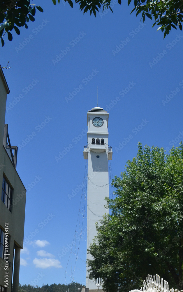 Obraz premium Modern White Clock Tower Standing Tall in Public City Park Under Clear Blue Sky