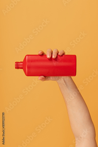 A hand holding a red bottle upside down with cap off