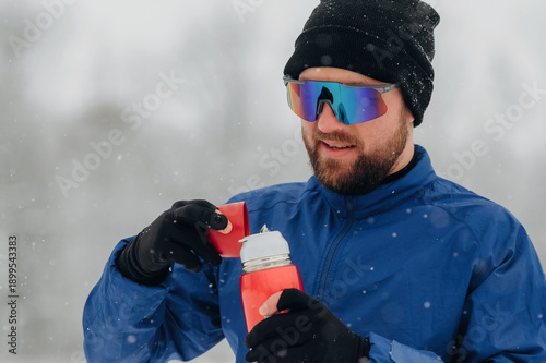 Photos Male athlete wearing sunglasses and winter clothing opens insulated water bottle