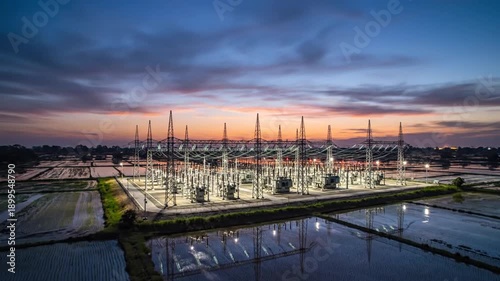 Cinematic aerial timelapse of a massive electrical power substation at dusk showing industrial energy infrastructure with glowing lights under a twilight sky in slow motion for utilities.