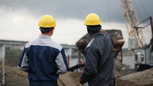 Two industry engineers caucasian and africa are controlling operation of crane on sand quarry.