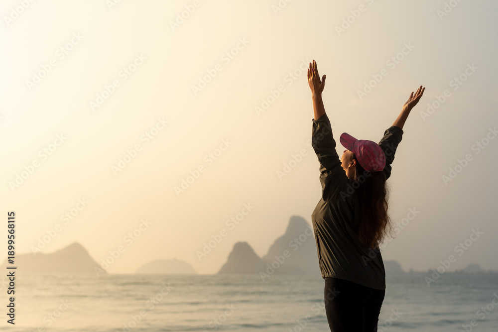Fototapeta premium Woman Raising Arms at Sunrise by the Sea with Mountains