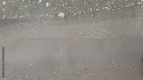 A close-up of the shore, water, and sand. The water rushing toward the shore, waves on the beach.