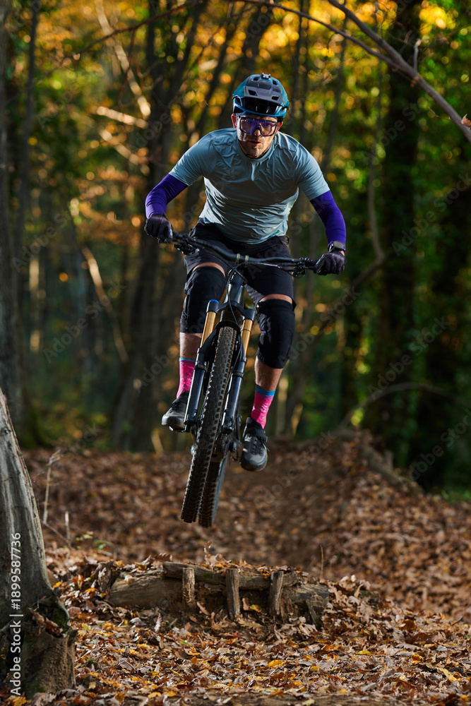 Fototapeta premium Intense Mountain Biker Jumping Over Log on Forest Trail During Autumn Ride
