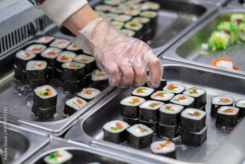 Buying sushi rolls in a store. A customer's hand in a disposable glove selects sushi rolls in a store.
