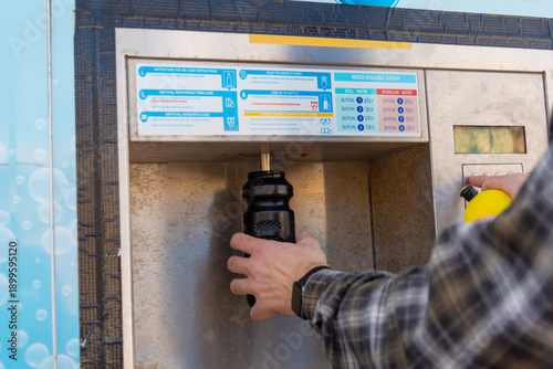 Foto Person refilling a reusable bottle at an outdoor public water dispenser