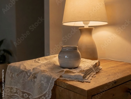 Cozy interior scene with ceramic vase on lace-covered wooden table near warm lamp