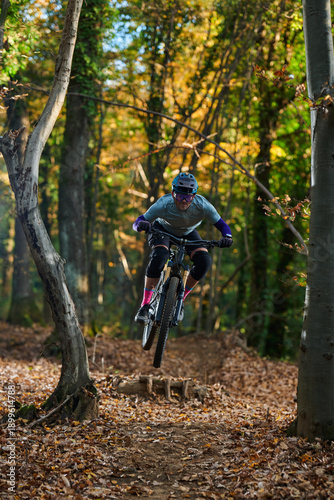 Mountain Biker Jumping Through An Autumn Forest Trail With Leaves Falling During Fall Adventure Experience