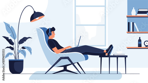 Relaxed man wearing headphones works on his laptop while sitting in a comfortable armchair in a stylish home office.