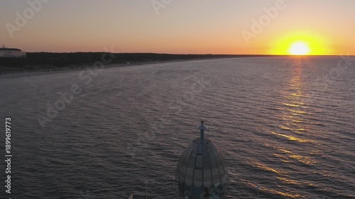 Picturesque sunset over the Baltic Sea. The low sun is reflected in the calm sea, while the endless sandy beach and the adjacent coastal forest are bathed in warm, golden light.