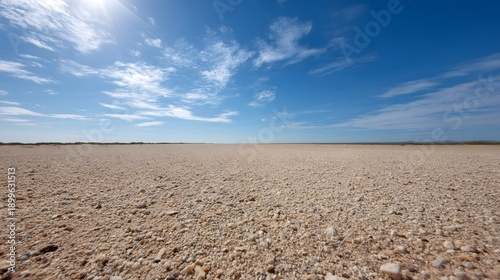 Expansive arid landscape with gravel ground under a bright blue sky with sun and clouds
