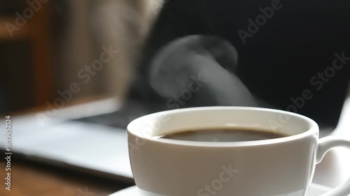 Steaming Cup of Hot Black Coffee on a Desk with Blurred Laptop