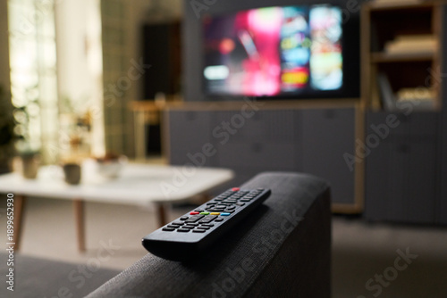 Cuadro en lienzo Remote control resting on sofa armrest with blurred television screen in backgro