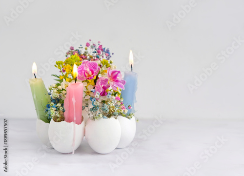 Easter or Ostara holidays concept. Beautiful decorative composition with burning candles and colorful flowers in eggs shells on table close up, light background. table decor for festive spring season