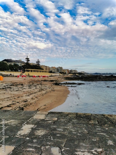 Boat on the beach. A scenic view of a beach with an orange umbrella on a cloudy day. Wooden boat on low tide. Beautiful views and nature. Sunumbrella on pier in storm and sea background.