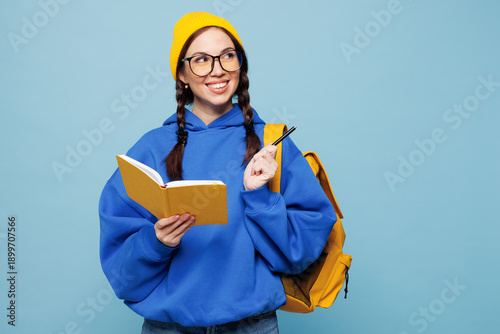 Foto Young smart woman student she wear casual clothes yellow backpack bag hold write down in exercise book diary notes isolated on pastel plain light blue color background