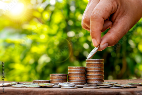 Close-up of a human hand placing a coin on a growing stack for financial growth and investment concept, business wealth management.