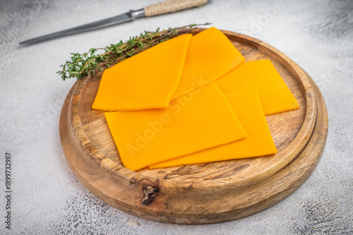 Fotografía Cheddar cheese slices arranged on wooden plate with kitchen knife light concrete