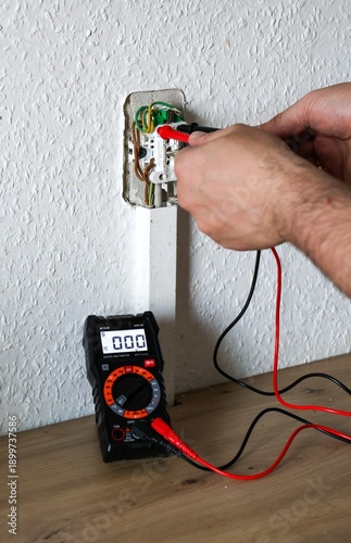 Foto Male hands using digital multimeter to check voltage of electrical socket during