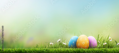 Three painted easter eggs celebrating a Happy Easter on a spring day with a green grass meadow, bright sunlight and a fresh spring background with copy space.
