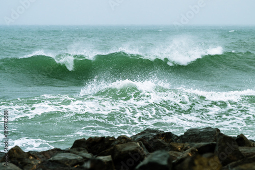 Fényképezés turbulent green ocean waves crashing onto a rocky shore, sending white foam and spray into the air