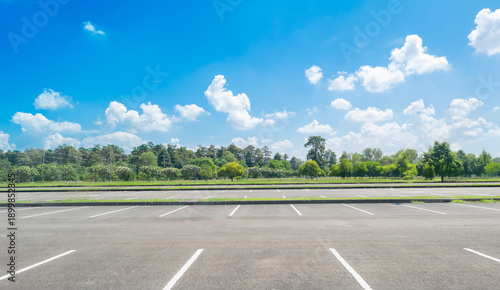 Wide empty asphalt parking lot background with white painted lines marked lens. Outdoor empty space parking lot with trees and cloudy sky. outside parking lot in a park