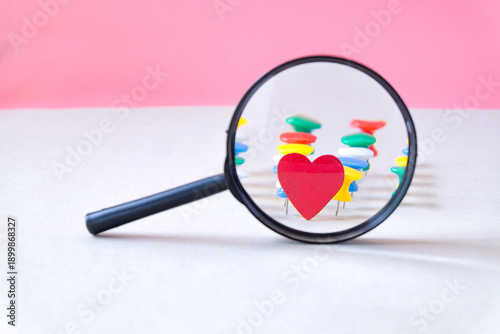 фотографія Magnifying glass on decorative red heart and push pin