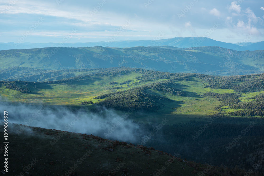 Ταπετσαρία Scenic aerial top view from above through low cloud on pass to green hilly vastness and layered mountain silhouettes far away under dramatic cloudy sky